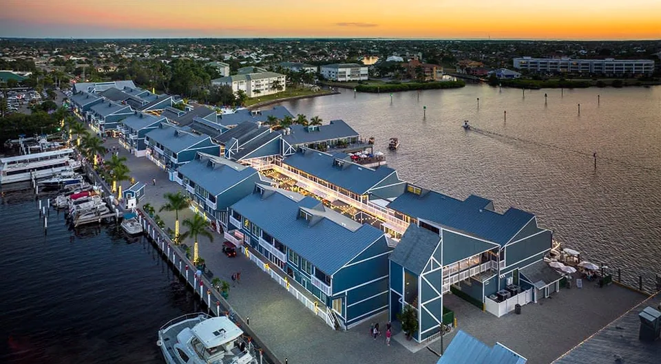 Fishermen's Village in Punta Gorda from the air at dusk: the blue tin roofs of the shops and restaurants on the pier, boats in the marina and Charlotte Harbor behind